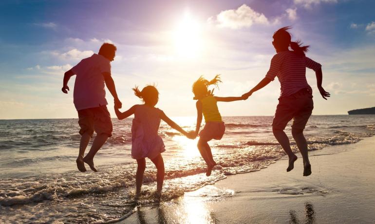 Glückliche Familie springt am Strand bei Sonnenuntergang.