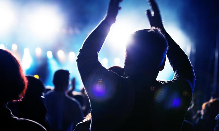Begeisterte Menge klatscht unter hellen Lichtern bei einem Konzert.