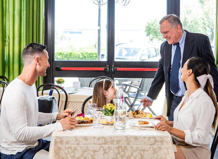 Familie beim Essen im Restaurant, Kellner lächelt.